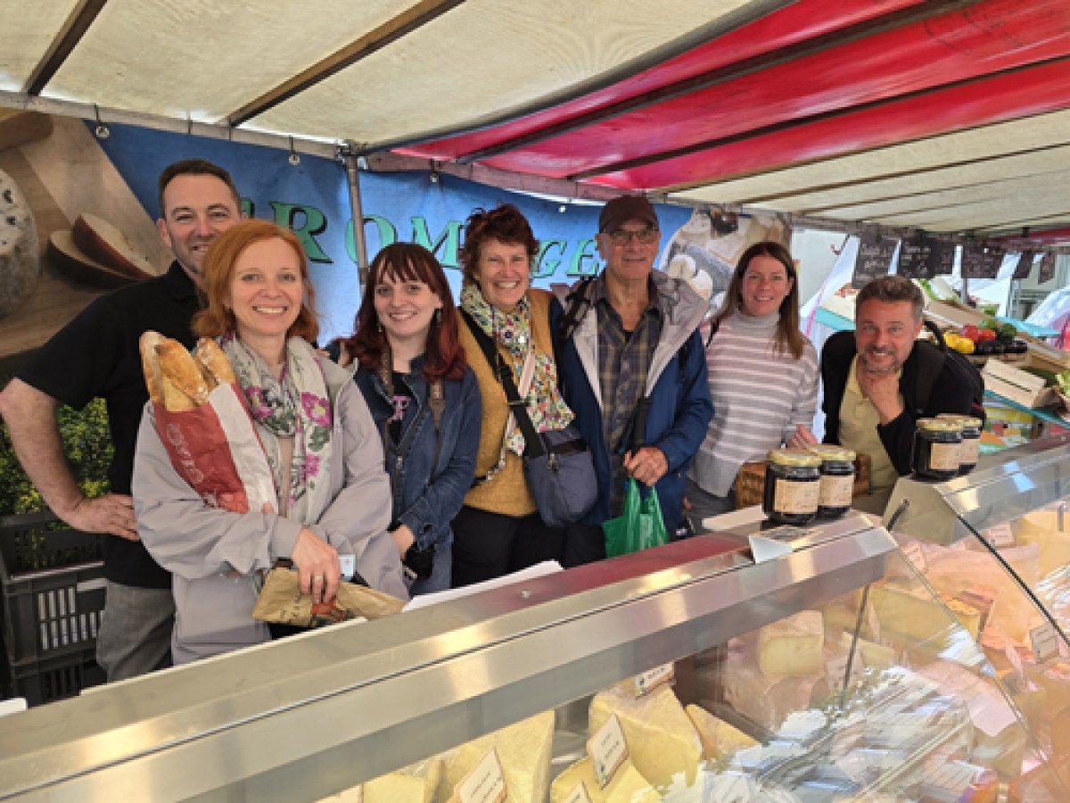 a group of people posing in front of tthe boutique of a cheese vendor at a parisian market